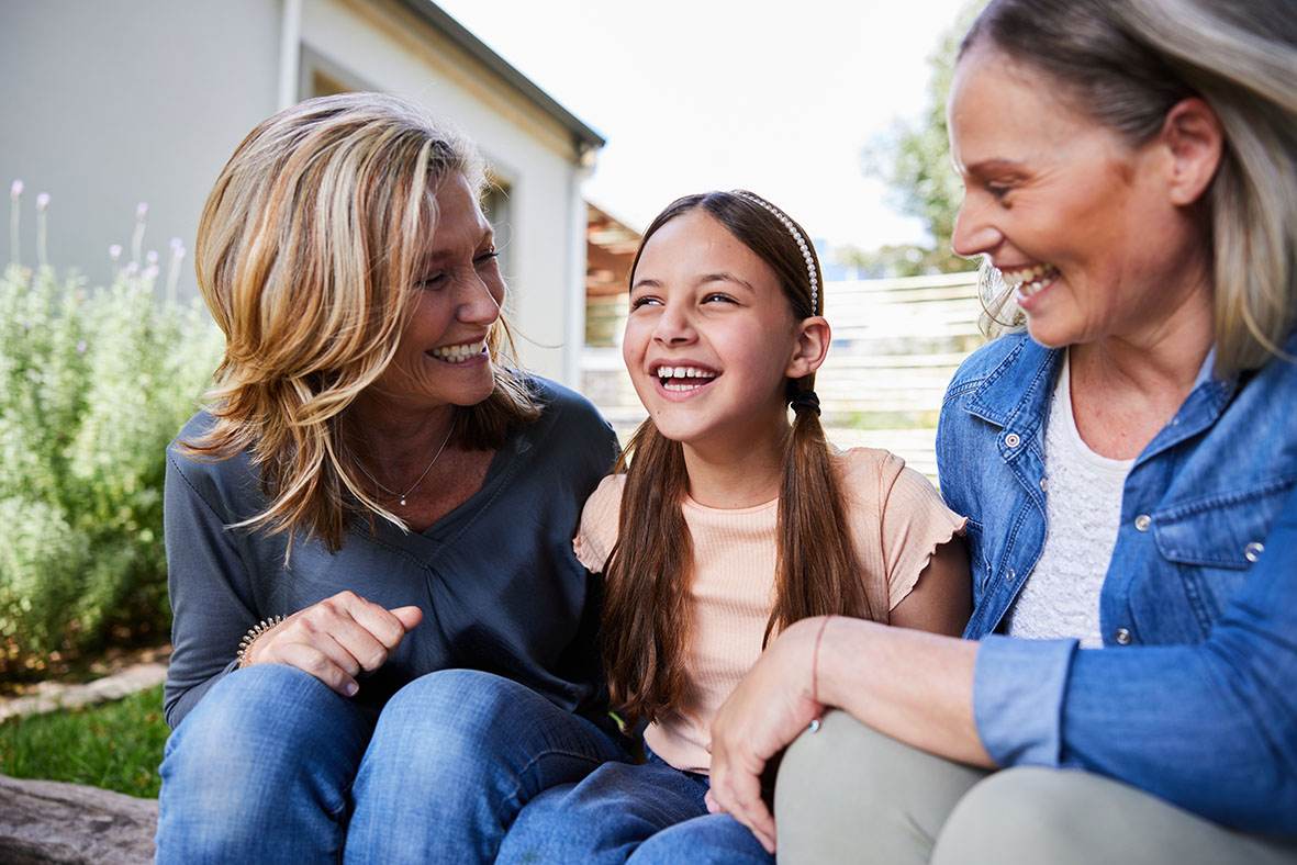 Laughing little girl sitting in a back yard with her mom and grandma