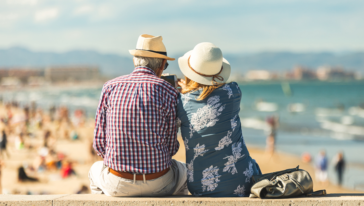 Two people sitting on a wall above the sand facing the beach